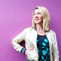 Blonde woman wearing a silver bomber jacket on a purple background